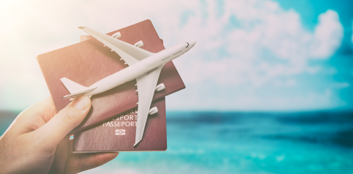 Passaportes em mãos junto com um avião em miniatura, com mar azul ao fundo